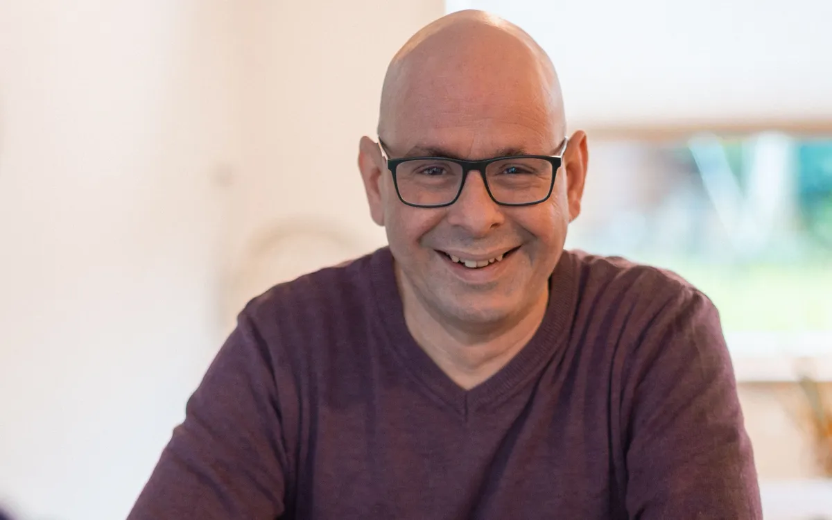 Roeland lachend aan een houten tafel tijdens een gesprek.