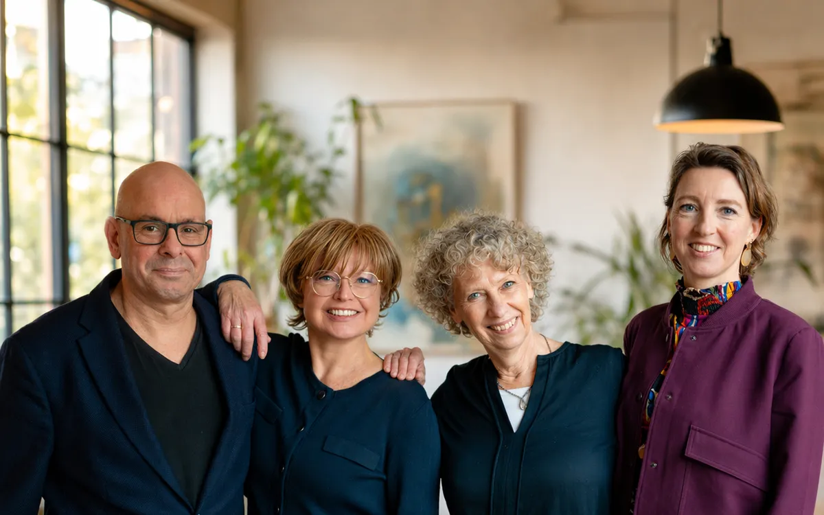 Roeland met drie collega's, lachend en arm in arm in een lichte ruimte.