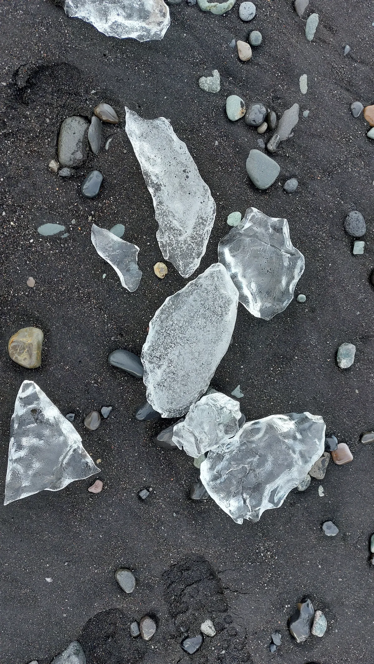 Kristalheldere ijsbrokken tussen donkere kiezels op zwart zand