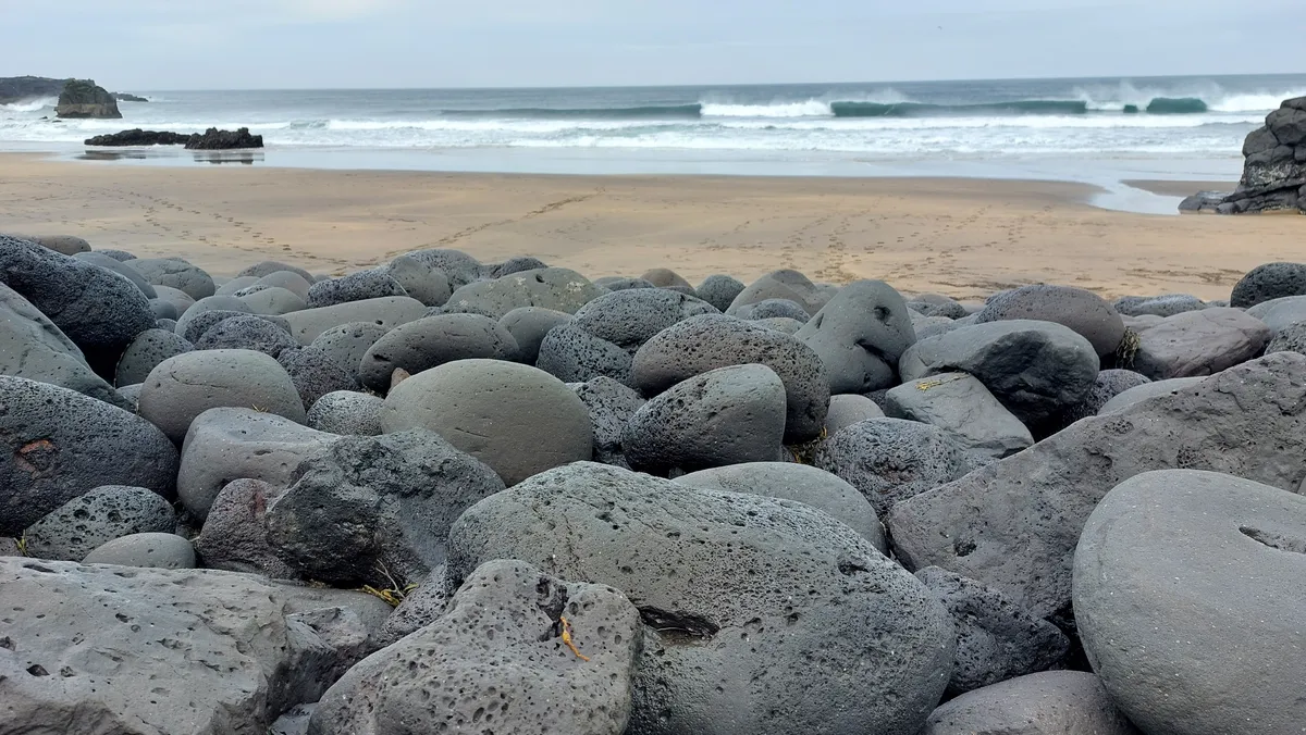 Ronde zwarte lavastenen op een strand met brekende golven